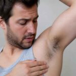 Mężczyzna w podkoszulku dotyka dłonią pachy i ogląda ją z niepokojem