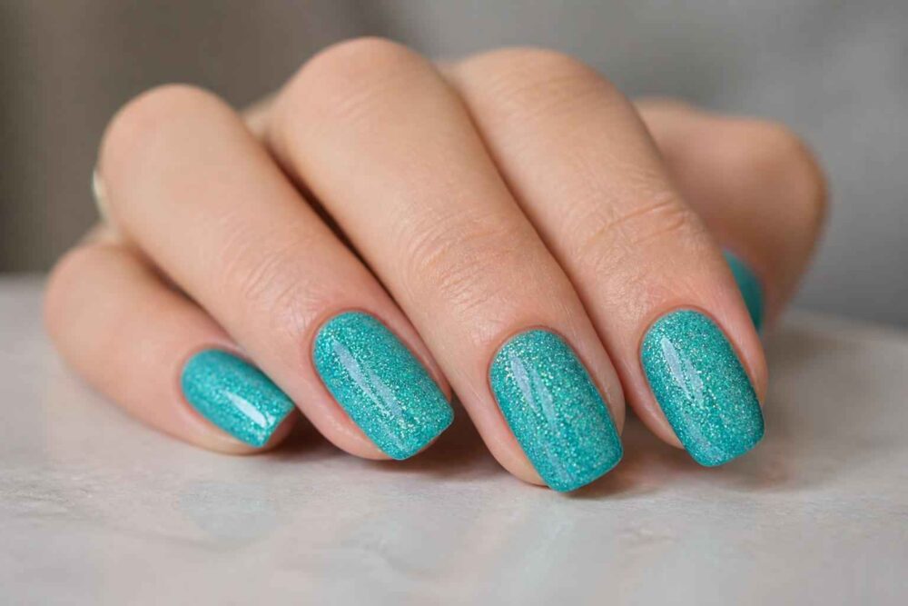 Dłoń z turkusowym manicure o błyszczącym wykończeniu na jasnym tle
